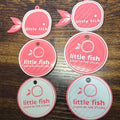 Set of 'little fish' branded round labels on a wooden surface